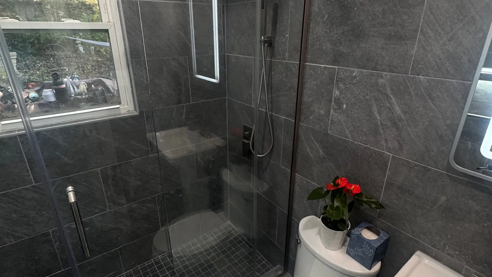 Remodelled bathroom in large-format grey stone tile with a glass shower and backlit mirror